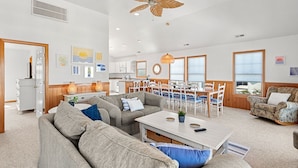 A spacious living room with a large sofa, a dining area with a table and chairs, and a ceiling fan.
