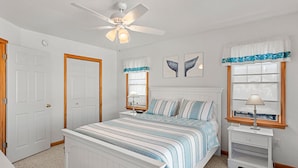 A bedroom with a bed, a nightstand, a ceiling fan, and two windows with curtains.