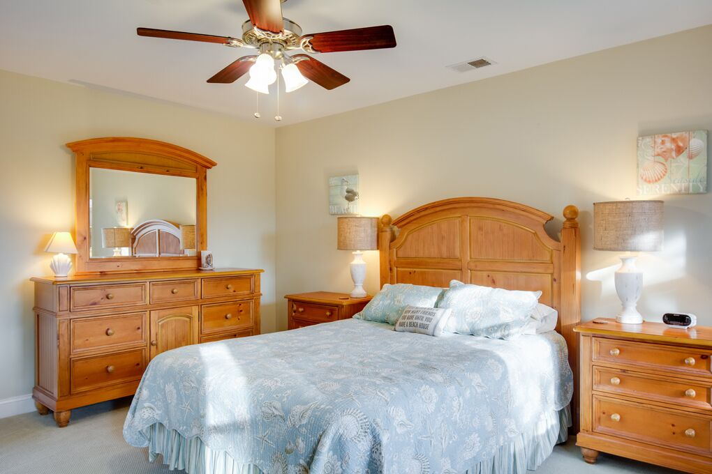 A bedroom with a bed, wooden dresser, nightstands, a ceiling fan, and wall art.