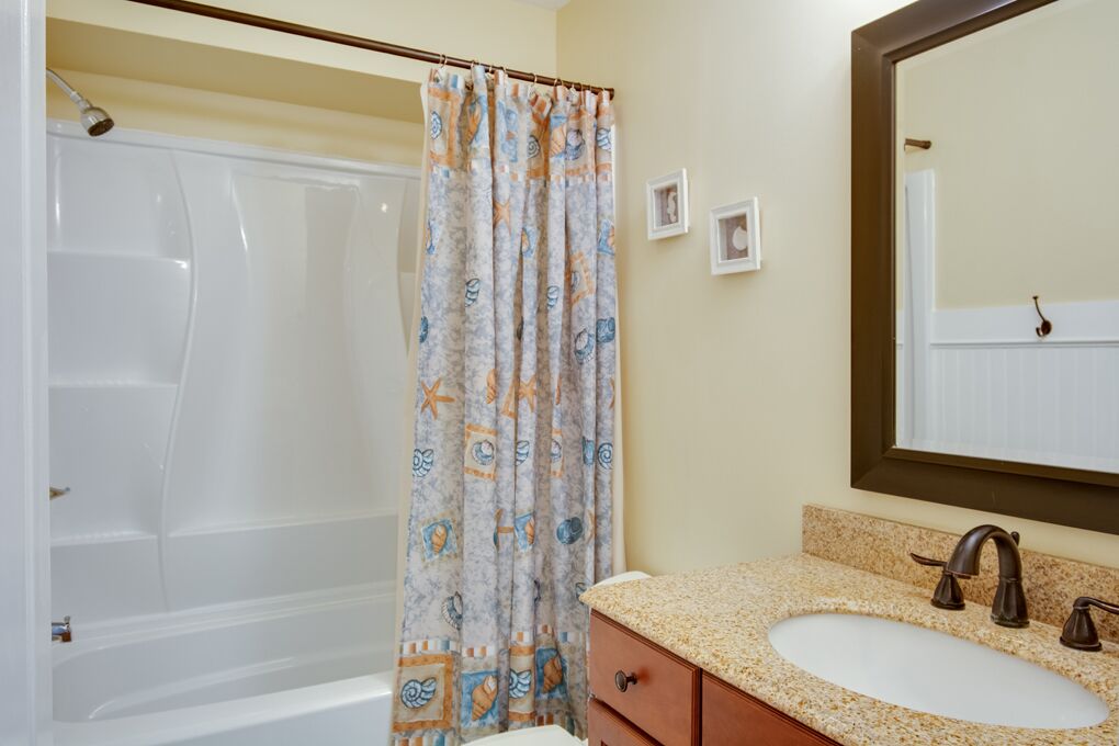 Un baño con bañera, cortina de ducha con estampado náutico, lavabo con encimera de granito y un espejo sobre el lavabo.