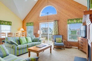 A cozy living room with a wooden ceiling, a large window, a sofa, a chair, and a coffee table.