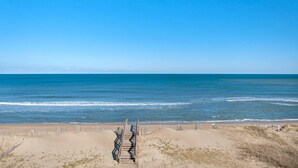A beach with a wooden walkway leading to the water, sandy dunes, and a clear blue sky. - Star of the Sea: Oceanfront Condo, Shared Pool (Kill Devil Hills)