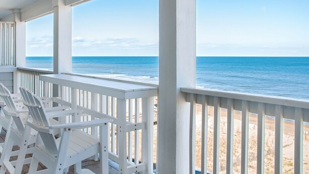 A covered outdoor seating area with white chairs and a view of the ocean. - Star of the Sea: Oceanfront Condo, Shared Pool (Kill Devil Hills)