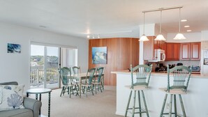 A modern kitchen with wooden cabinets, a dining area with a table and chairs, and a balcony with a view. - Daniel's Diamond: Oceanfront, Great Views, Pool (Nags Head)