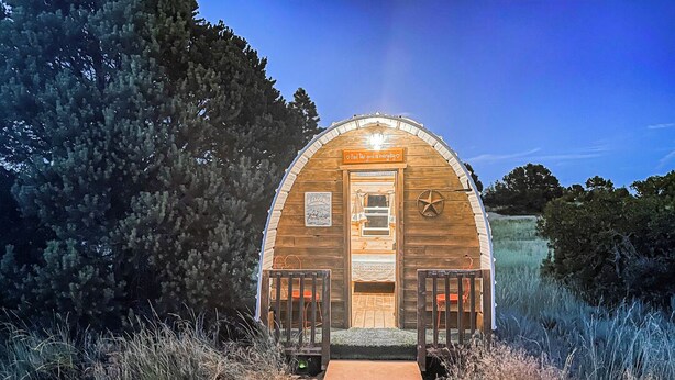 Une cabane en bois rustique, dotée d’une véranda, d’une porte et d’une petite fenêtre.