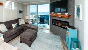 Uma sala de estar moderna com sofá seccional, lareira, TV na parede e vista para o oceano através de grandes janelas.