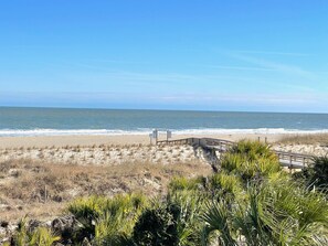 A beach with a wooden boardwalk leading to the ocean, surrounded by sand dunes and sparse vegetation.