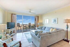 A living room with a sofa, TV, and a balcony with chairs.