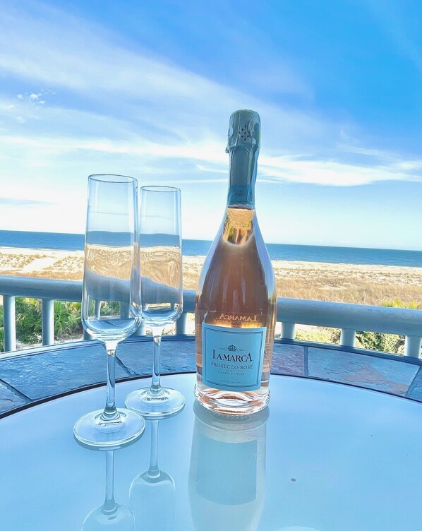 A bottle of Prosecco Rosé and two glasses on a table with a view of the beach.
