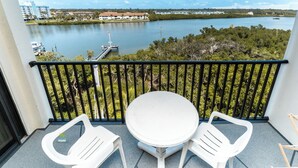 A balcony with a white table and two white chairs, overlooking a lake with buildings in the background. - Quiet Waters Condominium 5C (Indian Shores)