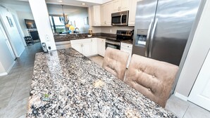 A modern kitchen with granite countertops, stainless steel appliances, and a tufted beige sofa. - Quiet Waters Condominium 5C (Indian Shores)