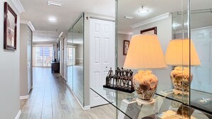 A hallway with a glass partition, a white door, and a glass table with decorative items.