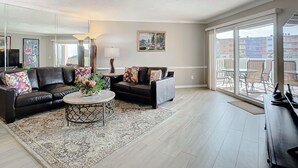 A spacious living room with a black leather sofa, a round coffee table, and a large mirror.