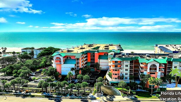 A beachfront hotel with colorful buildings, a parking area, and a view of the ocean.