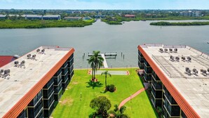 A high-rise building with multiple air conditioning units on the roof, a central courtyard with a palm tree, and a view of a body of water with a dock.