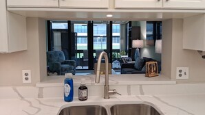 A modern kitchen with white cabinets, a double sink, and a view of a living area with a sofa and a table.