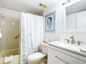 Een badkamer met douche, toilet, wastafel en een ingelijste foto aan de muur.
