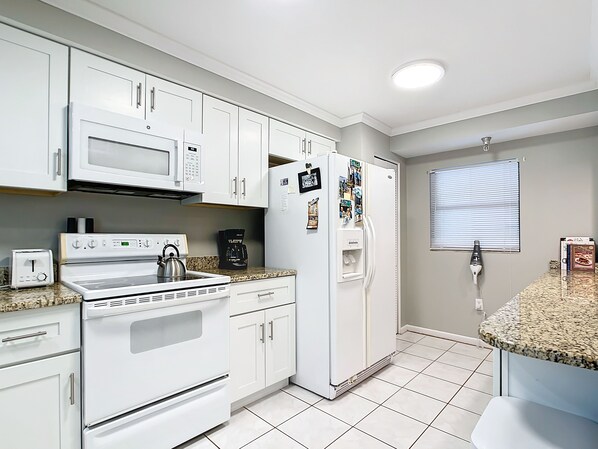 A kitchen with white cabinets, a microwave, a stove, a refrigerator, and a coffee maker.