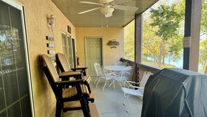 Eine überdachte Terrasse mit Sitzgelegenheiten im Freien, einem Deckenventilator und Blick auf Bäume und einen See.