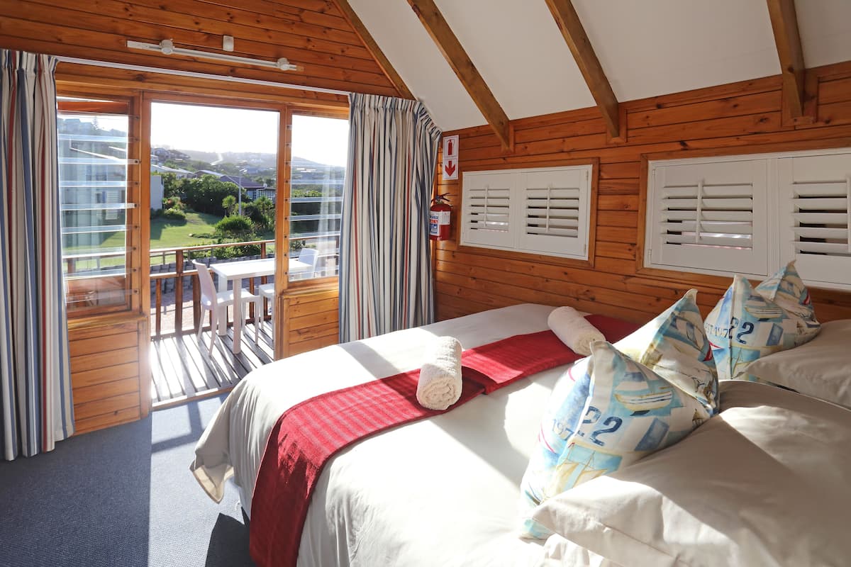 Ein Schlafzimmer mit einem großen Bett, einer roten Decke und Blick auf einen Balkon mit Tisch und Stühlen.