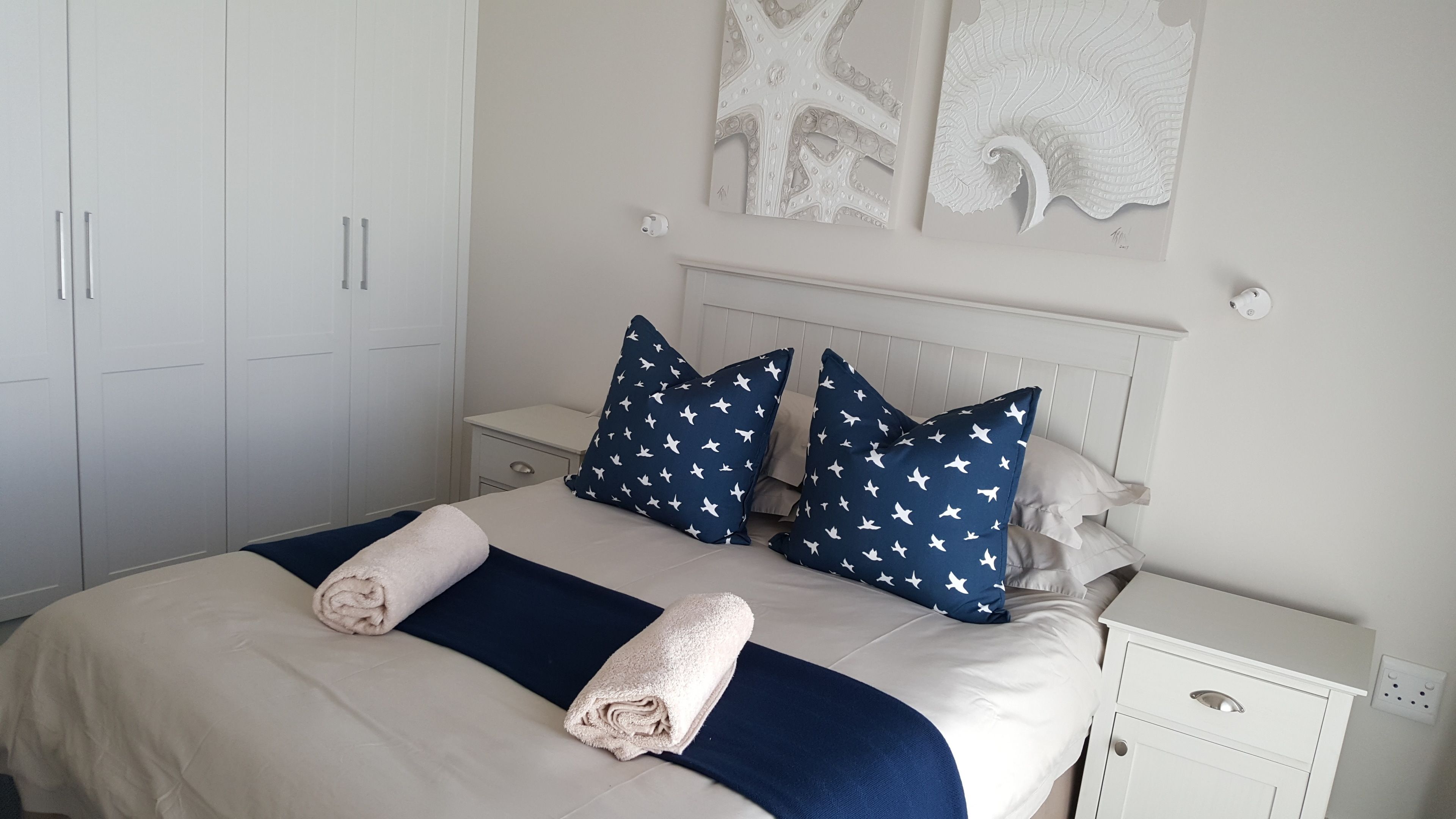 A neatly made bed with two pillows, a bedside table, and a wardrobe.
