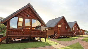 A row of log cabins with wooden decks and large windows, each with a distinct number. - Brenton On Sea Cottages (Knysna)