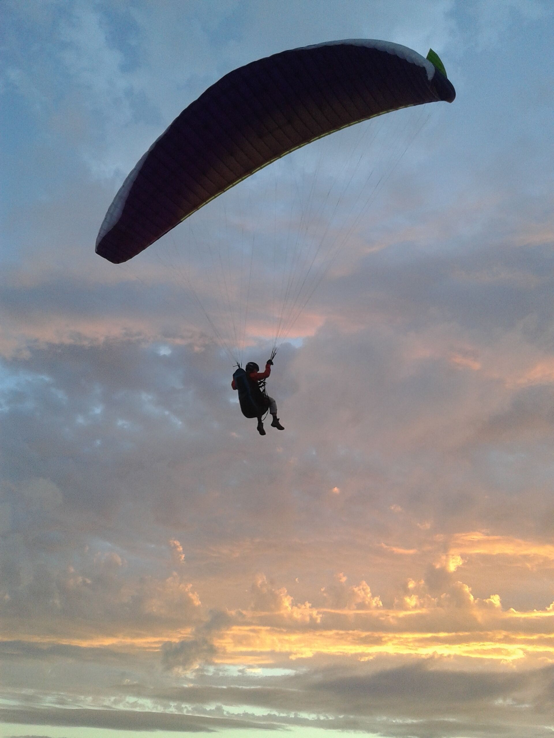 A person paragliding with a large wing against a sunset sky.