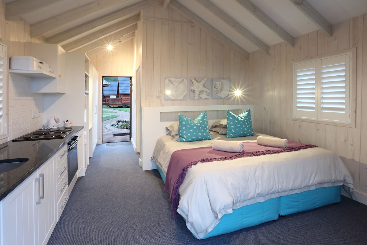 Ein Schlafzimmer mit einem Bett, einem Nachttisch, einem eingebauten Schreibtisch und einem Fenster mit Jalousien.