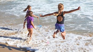 Two children playing in the shallow water at the beach with a rocky outcrop in the background. - Brenton On Sea Cottages (Knysna)