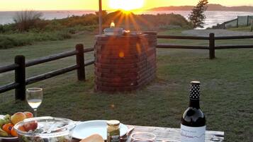 A picnic setup with a bottle of wine, glasses, a salad bowl, and a cheese plate on a wooden table.
