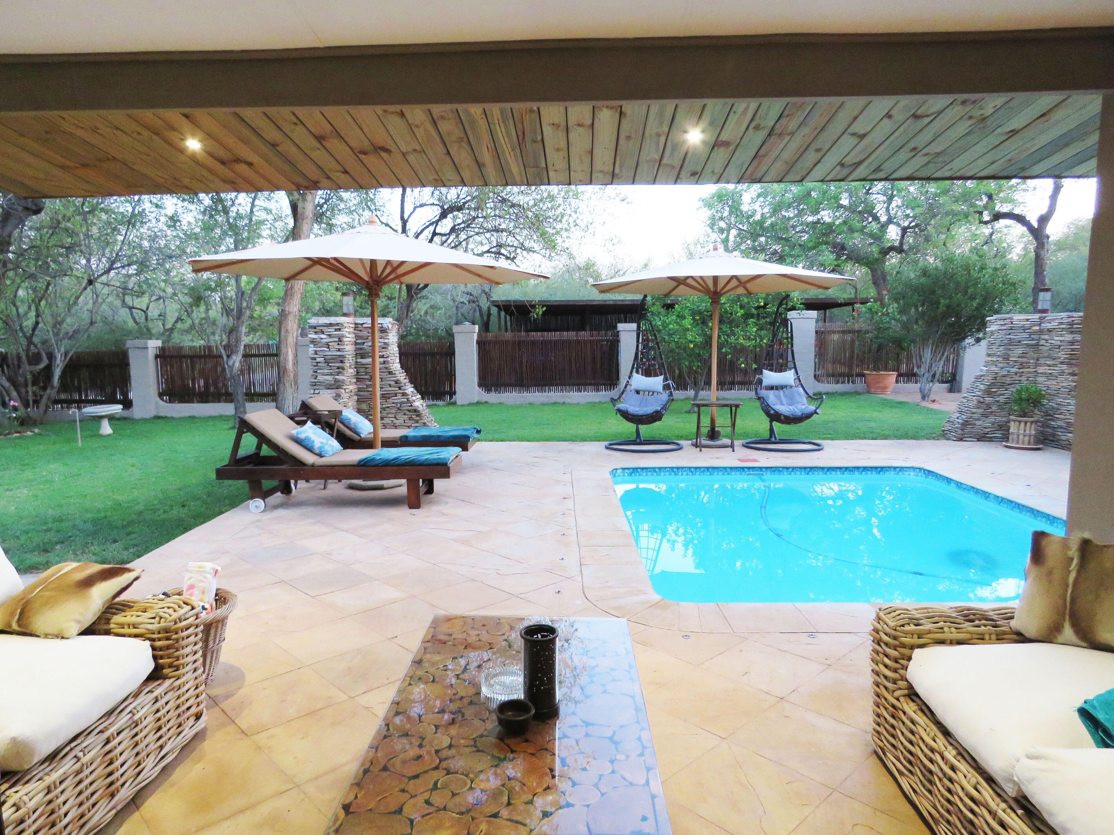 A backyard with a swimming pool, two wicker lounge chairs, a table, and a stone wall.