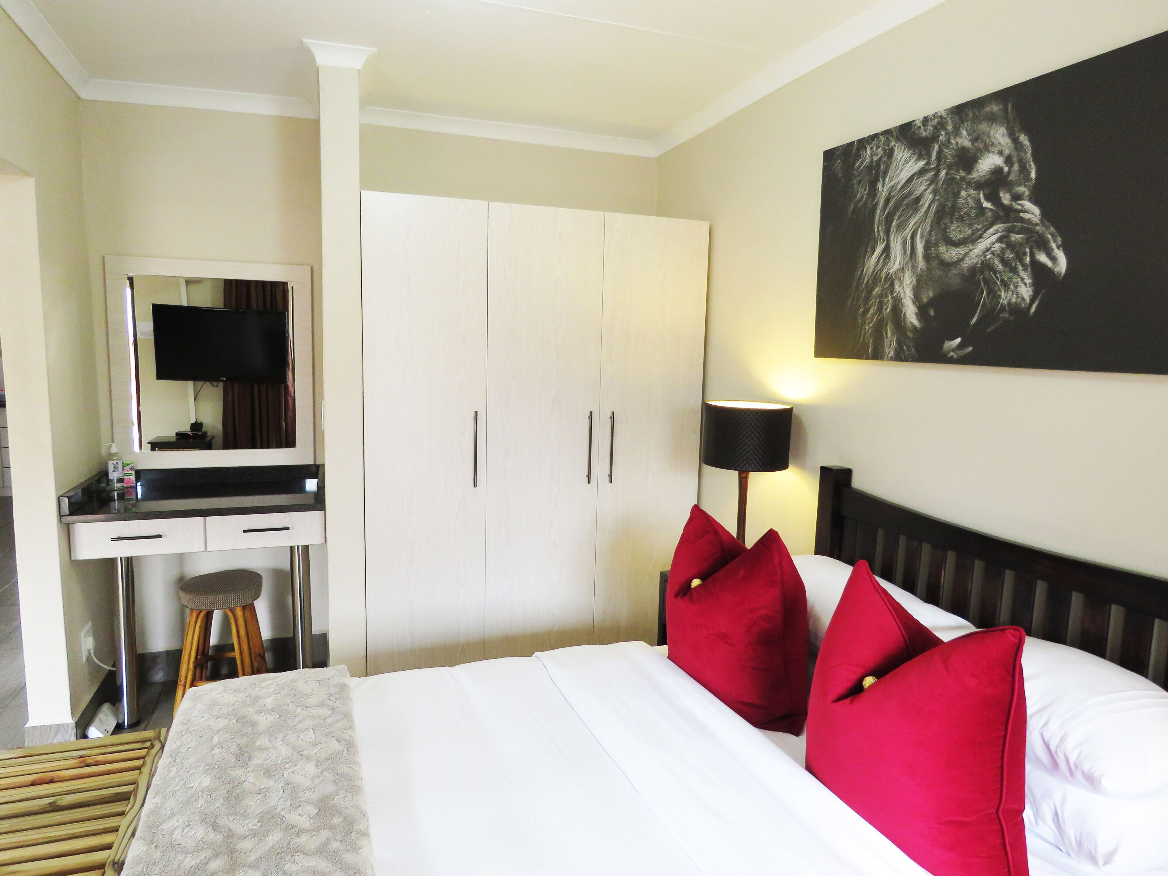 Una habitación de hotel con una cama, un escritorio con espejo, un televisor y un cuadro en la pared.