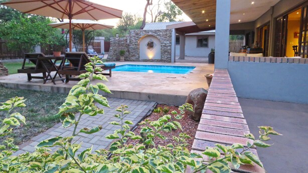 A backyard with a swimming pool, patio furniture, and a stone wall. - Wild Dog Guest Lodge (Hoedspruit)
