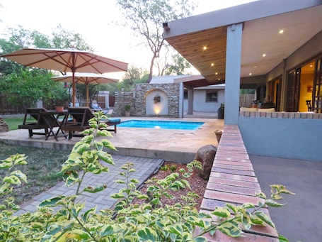 A backyard with a swimming pool, patio furniture, and a stone wall.