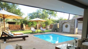 A backyard with a swimming pool, lounge chairs, and umbrellas. - Wild Dog Guest Lodge (Hoedspruit)
