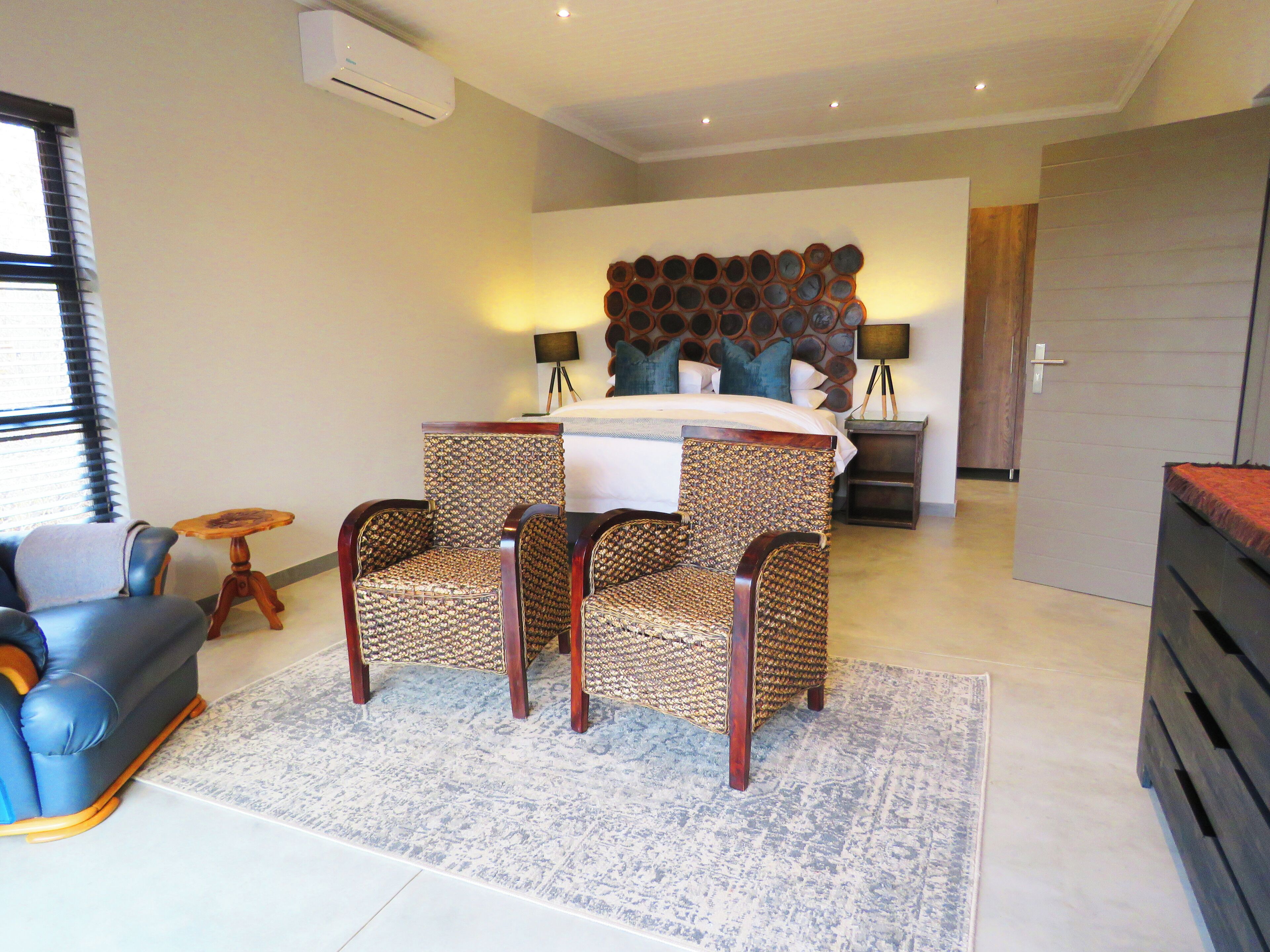 A bedroom with a bed, two chairs, a small table, a lamp, and a wardrobe.