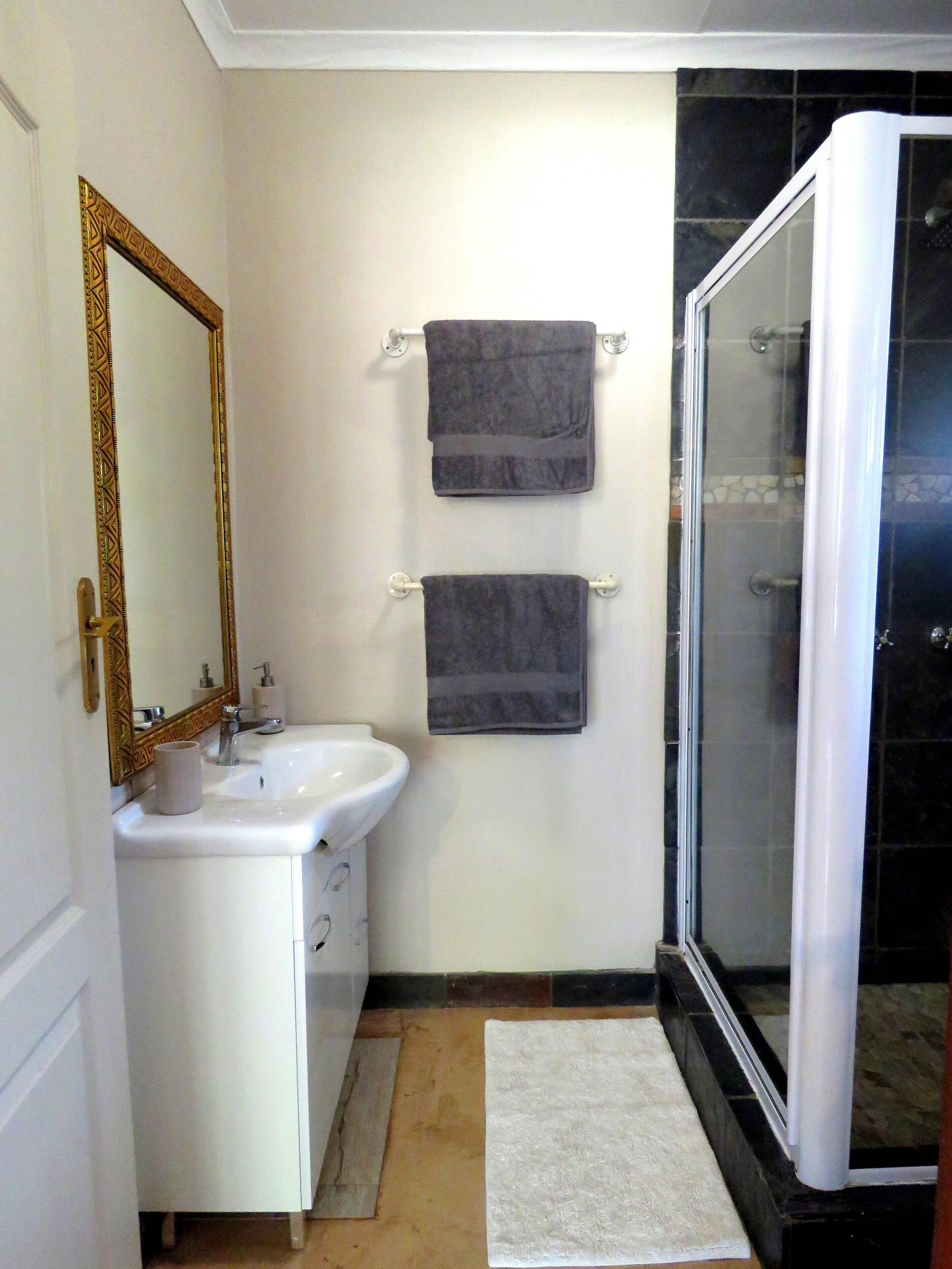 A bathroom with a white sink, a mirror with a decorative frame, two towels hanging on hooks, and a glass-enclosed shower.