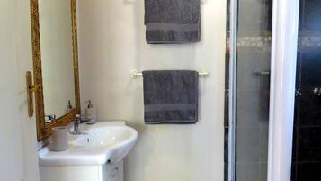 A bathroom with a white sink, a mirror with a decorative frame, two towels hanging on hooks, and a glass-enclosed shower.