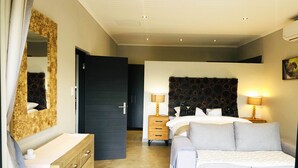 A modern bedroom with a bed, bedside tables, a dresser, a mirror, and a door. - Wild Dog Guest Lodge (Hoedspruit)