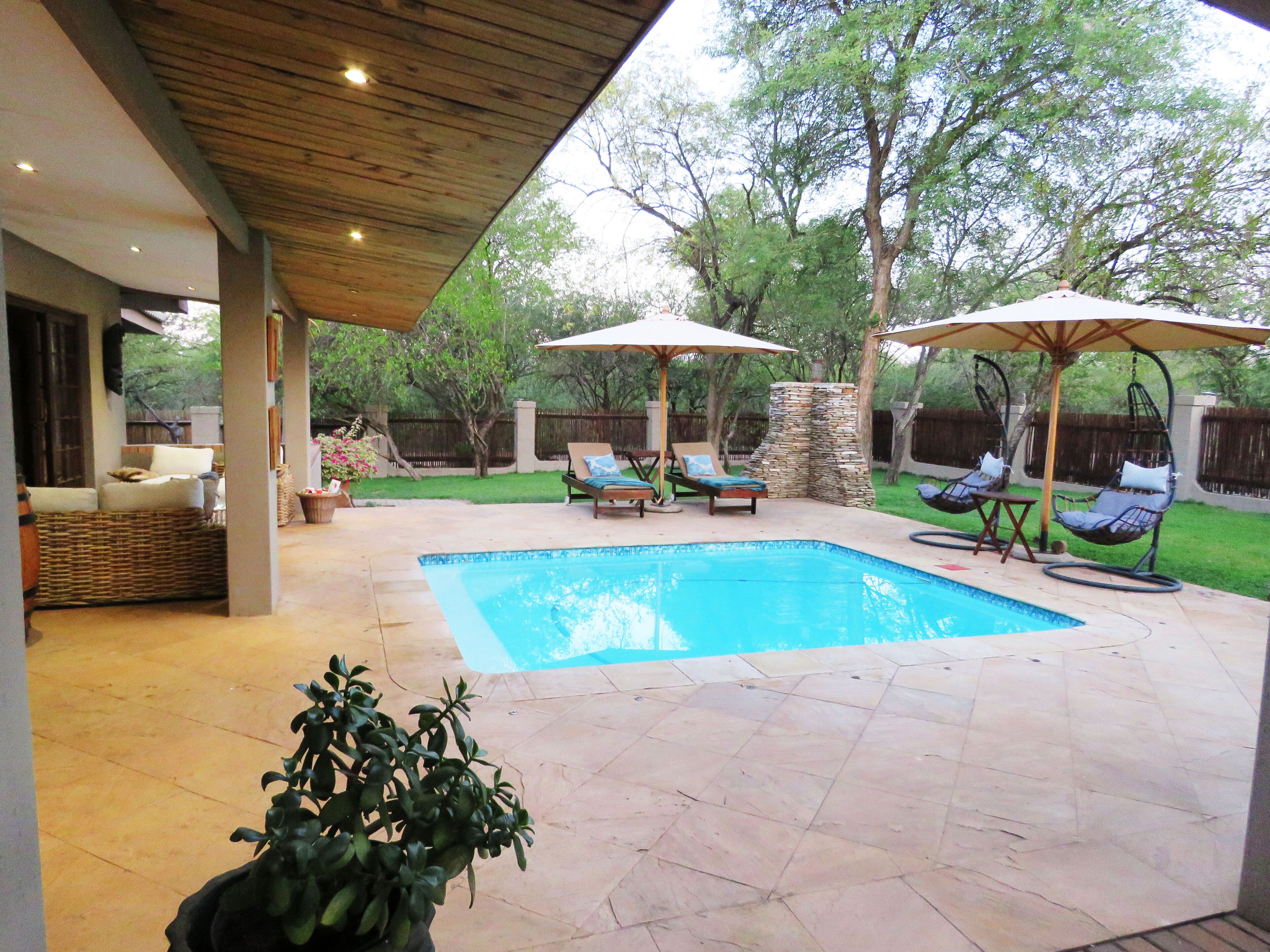 A backyard with a swimming pool, covered seating areas, and a stone wall.
