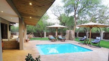 A backyard with a swimming pool, covered seating areas, and a stone wall.