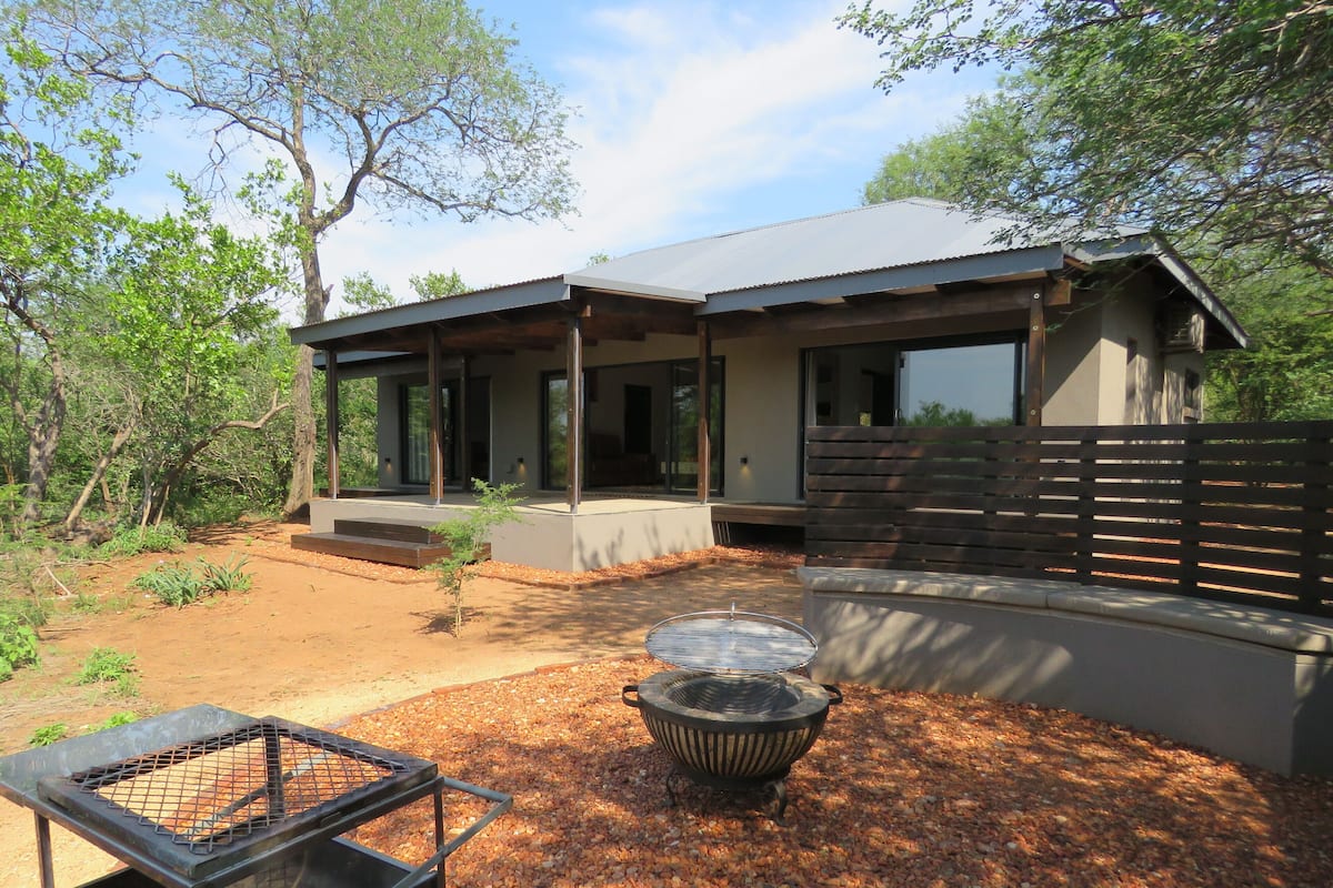 Ein modernes Haus mit überdachter Terrasse, Feuerstelle und Grillplatz.