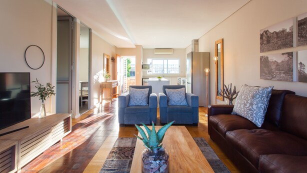 A modern living room with a TV, sofa, and coffee table. There is a kitchen in the background with a dining area. - 109 on Dorp (Stellenbosch)