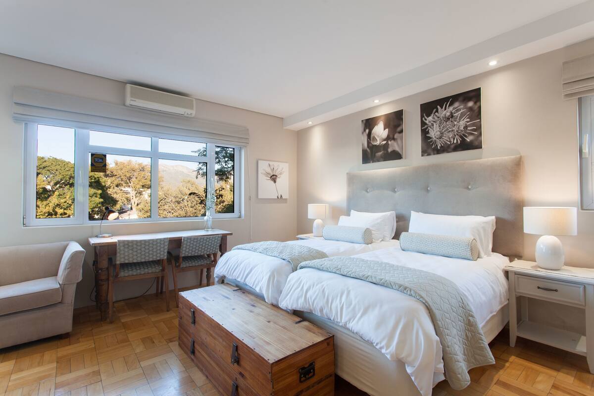 A bedroom with a large bed, a desk, and a view of trees through the window.