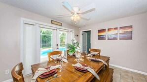 Comedor con una mesa de madera dispuesta para seis comensales, un ventilador de techo y vistas al exterior a través de un ventanal.