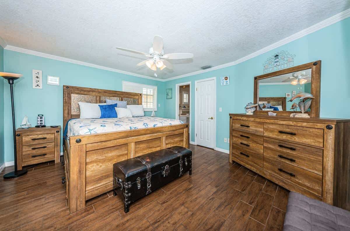 Een slaapkamer met een houten bed, een bankje, een dressoir en een plafondventilator.