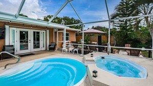 Un área de piscina con jacuzzi, asientos al aire libre y un porche cubierto.