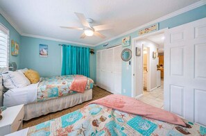A bedroom with two beds, a ceiling fan, a bathroom visible through an open door, and a hallway leading to other rooms.