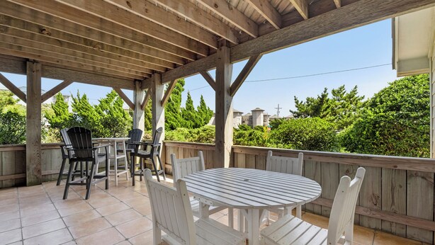 Una terrazza esterna con una pergola in legno, un tavolo rotondo e sedie bianche.