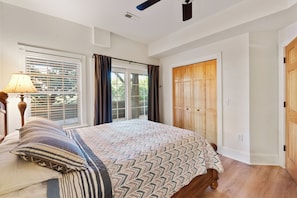 Un dormitorio con una cama grande, una mesita de noche, una lámpara, una ventana con persianas y un armario de madera.
